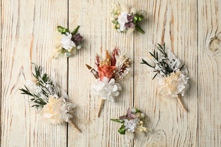 Stylish boutonnieres on light wooden table, flat lay