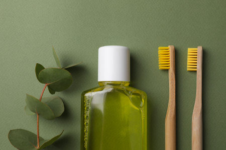 Fresh mouthwash in bottle, toothbrushes and eucalyptus branch on green background, flat layの写真素材