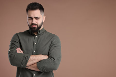 Portrait of sad man with crossed arms on brown background, space for textの写真素材