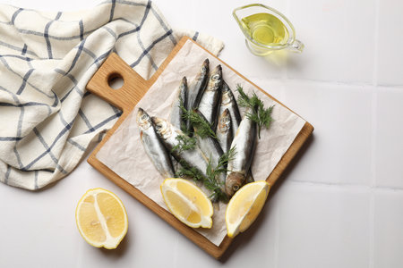 Fresh raw sprats, dill, oil and cut lemon on white tiled table, flat layの写真素材