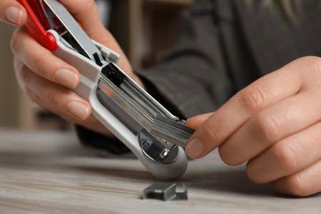Woman putting metal staples into stapler at wooden table, closeupの写真素材