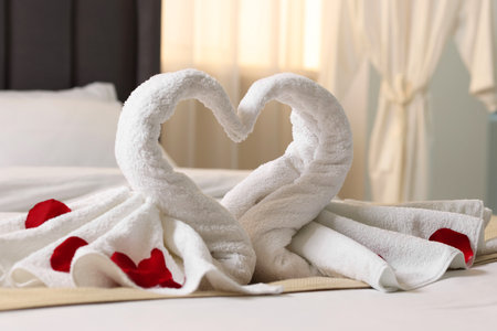 Honeymoon. Swans made of towels and rose petals on bed in roomの写真素材