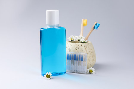 Composition with fresh mouthwash in bottle, toothbrushes and interdental brushes on gray backgroundの写真素材
