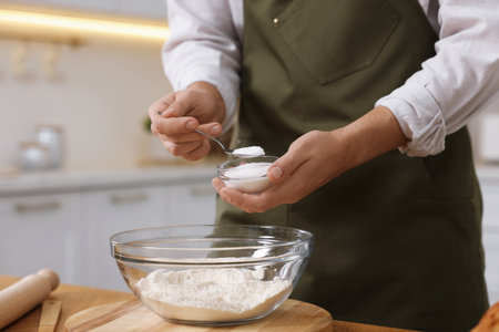 Making bread. Man putting salt into bowl with flour at wooden table in kitchen, closeupの写真素材
