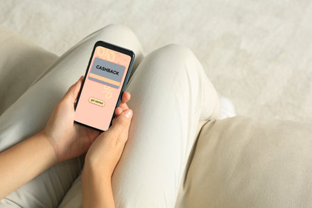 Cashback. Woman holding smartphone indoors, closeup. Illustration of credit card and percent signs on device screenの写真素材
