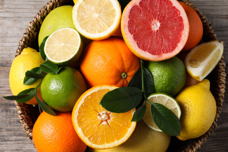 Different fresh citrus fruits and leaves in wicker basket on wooden table, top viewの写真素材