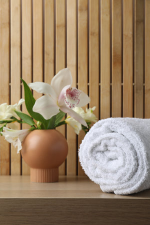 Rolled terry towel and beautiful flowers on wooden tableの写真素材