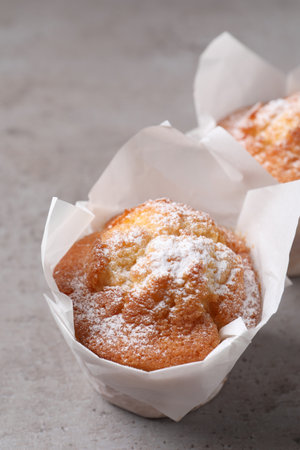 Delicious muffins with powdered sugar on gray table, closeup