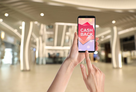 Woman using smartphone with word Cashback and shopping cart icon indoors, closeup. Space for textの写真素材