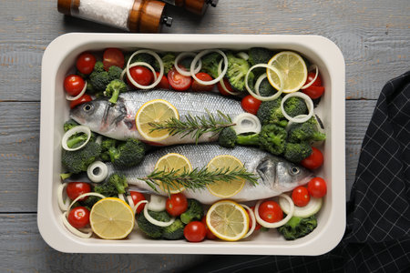 Raw fish with vegetables and lemon in baking dish on gray wooden table, top viewの写真素材