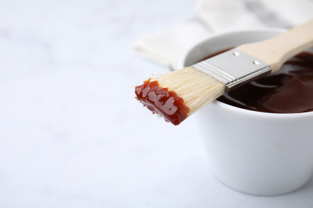Marinade in bowl and basting brush on white table, closeup. Space for textの写真素材