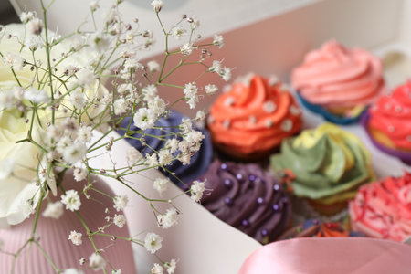 Different colorful cupcakes in box and flowers on table, closeupの写真素材
