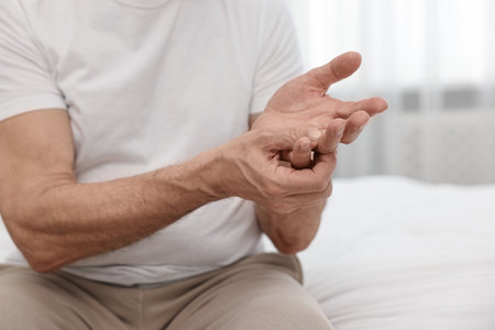 Arthritis symptoms. Man suffering from pain in hand on bed at home, closeupの写真素材
