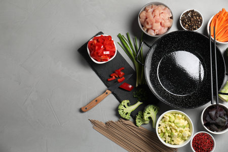 Wok pan, noodles, chicken and other products on light gray table, flat lay. Space for textの写真素材