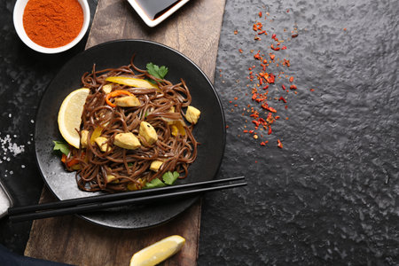 Stir-fry. Tasty noodles with vegetables and meat served on dark textured table, flat lay. Space for...