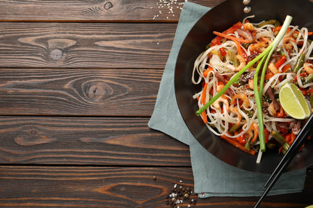 Shrimp stir fry with noodles and vegetables in wok on wooden table, top view. Space for textの写真素材