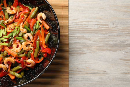 Shrimp stir fry with vegetables in wok on wooden table, top view. Space for textの写真素材