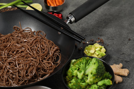 Wok with noodles and other products on gray table