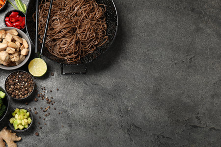 Wok with noodles, chicken and other products on gray table, flat lay. Space for text