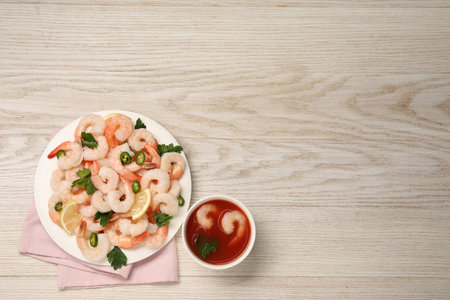 Tasty boiled shrimps with sauce cocktail, chili, parsley and lemon on light wooden table, flat lay. Space for textの写真素材