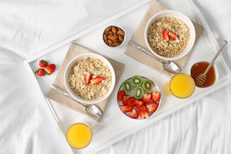 Tasty breakfast served in bed. Oatmeal, juice, fruits, almonds and honey on tray, top viewの写真素材