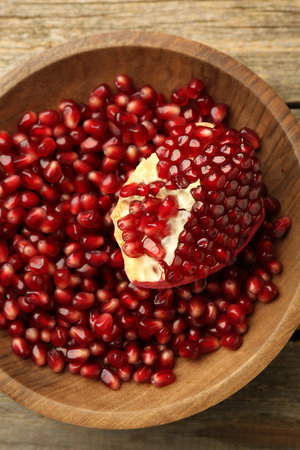 Ripe juicy pomegranate grains in bowl on wooden table, top viewの写真素材