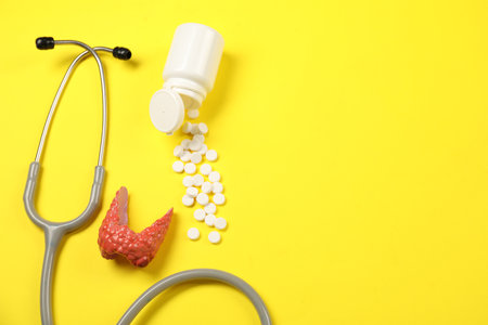 Endocrinology. Stethoscope, bottle with pills and model of thyroid gland on yellow background, flat lay. Space for textの写真素材