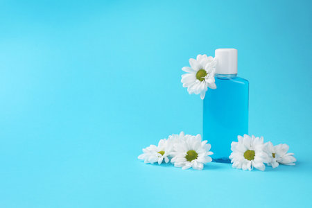 Fresh mouthwash in bottle and flowers on light blue background. Space for textの写真素材