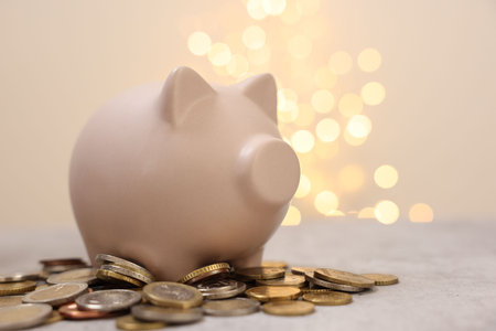 Piggy bank and coins on gray table against blurred lightsの写真素材