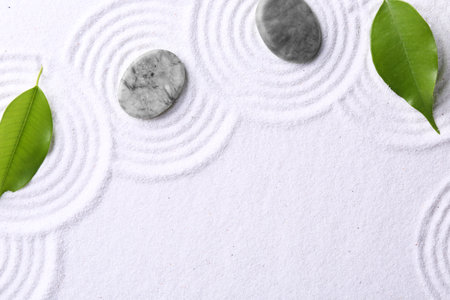 Zen garden stones and green leaves on white sand with pattern, flat lay. Space for textの写真素材