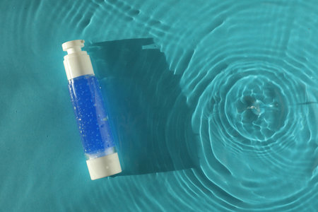 Bottle of cosmetic product in water on turquoise background, top view. Space for text