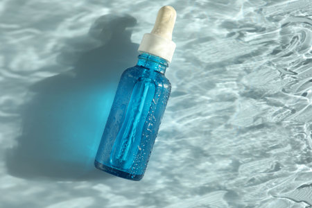 Wet bottle of cosmetic serum on light blue background, top view. Space for textの写真素材