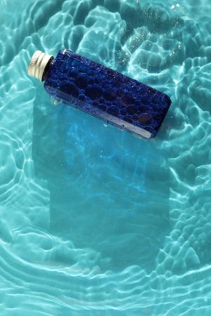 Bottle of cosmetic product in water on turquoise background, top view. Space for textの写真素材