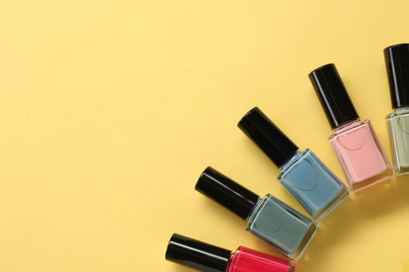 Colorful nail polishes in bottles on yellow background, flat lay. Space for textの写真素材
