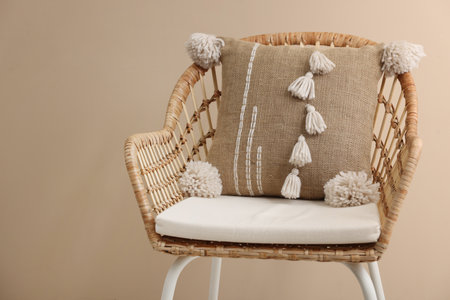 Stylish soft pillow on armchair near beige wall. Space for text