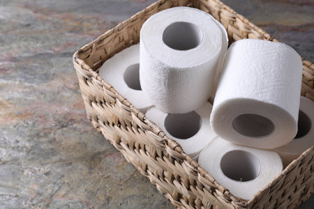 Toilet paper rolls in wicker basket on textured table, space for textの写真素材