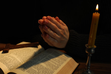 Woman praying at table with burning candle and Bible, closeupの写真素材