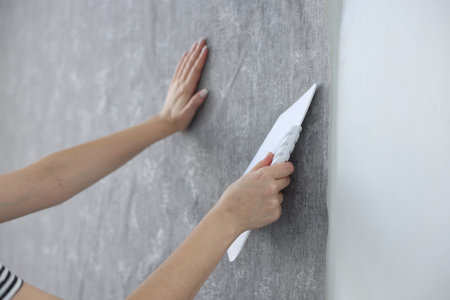 Woman smoothing stylish gray wallpaper in room, closeupの写真素材