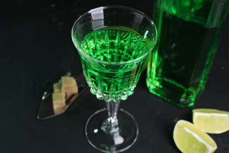 Absinthe in glass, spoon, brown sugar and lime on black table, closeup. Alcoholic drinkの写真素材