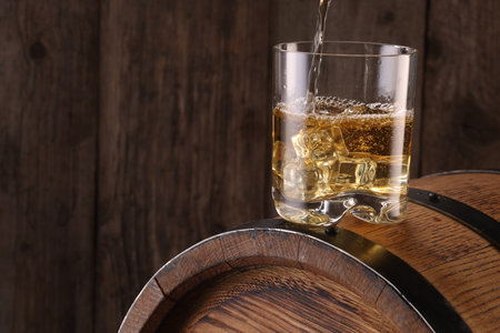Pouring whiskey into glass on barrel against wooden background, closeup. Space for textの写真素材