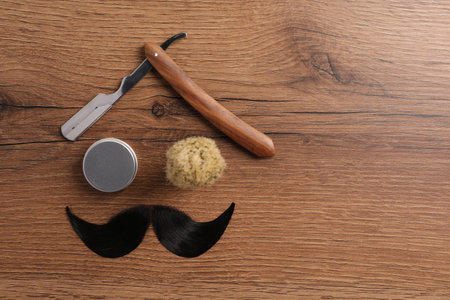 Artificial moustache and barber tools on wooden table, flat lay. Space for textの写真素材