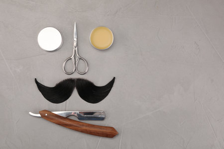 Artificial moustache and barber tools on gray table, flat lay. Space for textの写真素材