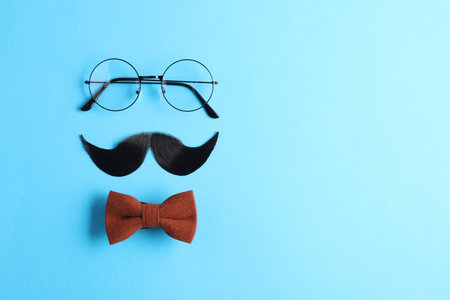 Artificial moustache, bowtie and glasses on light blue background, flat lay. Space for textの写真素材