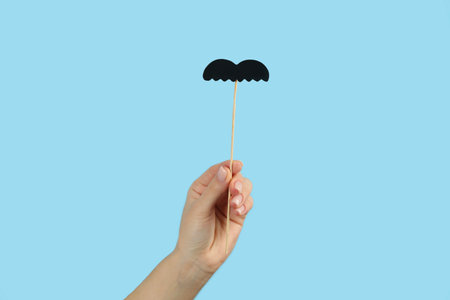 Woman with fake paper mustache on light blue background, closeupの写真素材