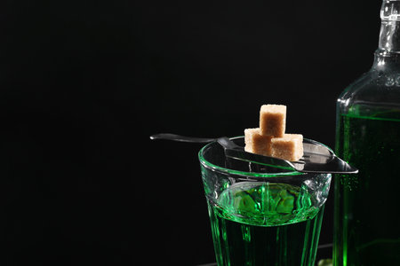 Absinthe in glass, brown sugar and spoon against black background, space for text. Alcoholic drinkの写真素材