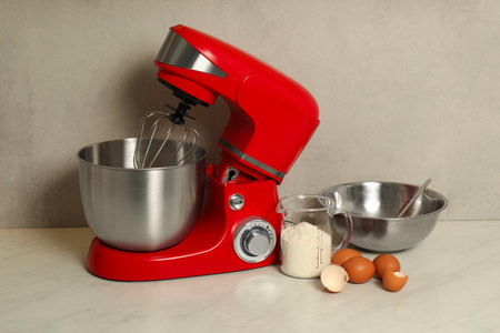 Modern red stand mixer, eggs, container with flour and bowl on white marble tableの写真素材