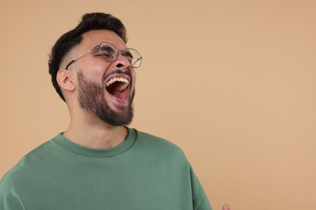 Handsome young man laughing on beige background, space for textの写真素材