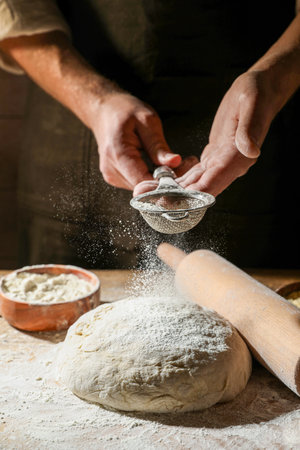 Man sprinkling flour over dough at wooden table, closeupの写真素材