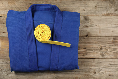 Yellow karate belt and blue kimono on wooden background, top view. Space for textの写真素材