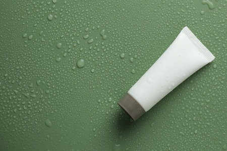 Moisturizing cream in tube on green background with water drops, top view. Space for textの写真素材